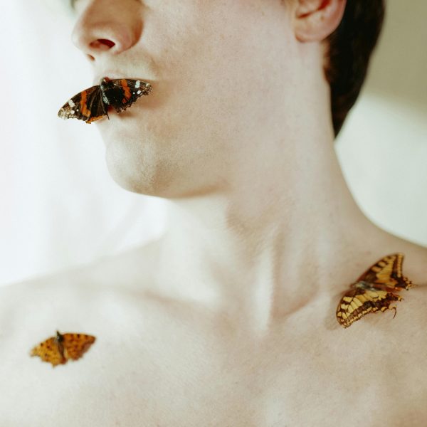 Männliches Gesicht und Oberkörper teils nackt, mit drei Pfauenaugen-Schmetterlingen.