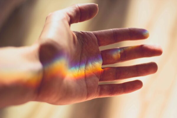 ausgestreckte Hand, in der sich ein Regenbogen zeigt